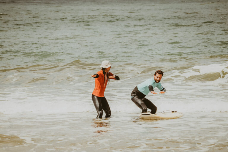 Surflehrerin zeigt Schüler im Surfkurs auf Sylt wie man im Wasser richtig steht.